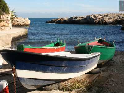 Le tipiche barche dei pescatori, colorate di verde e rosso o bianco e blu, sono ormeggiate su una spiaggia di pietre e ciottoli chiari che si stempera in un meraviglioso mare blu